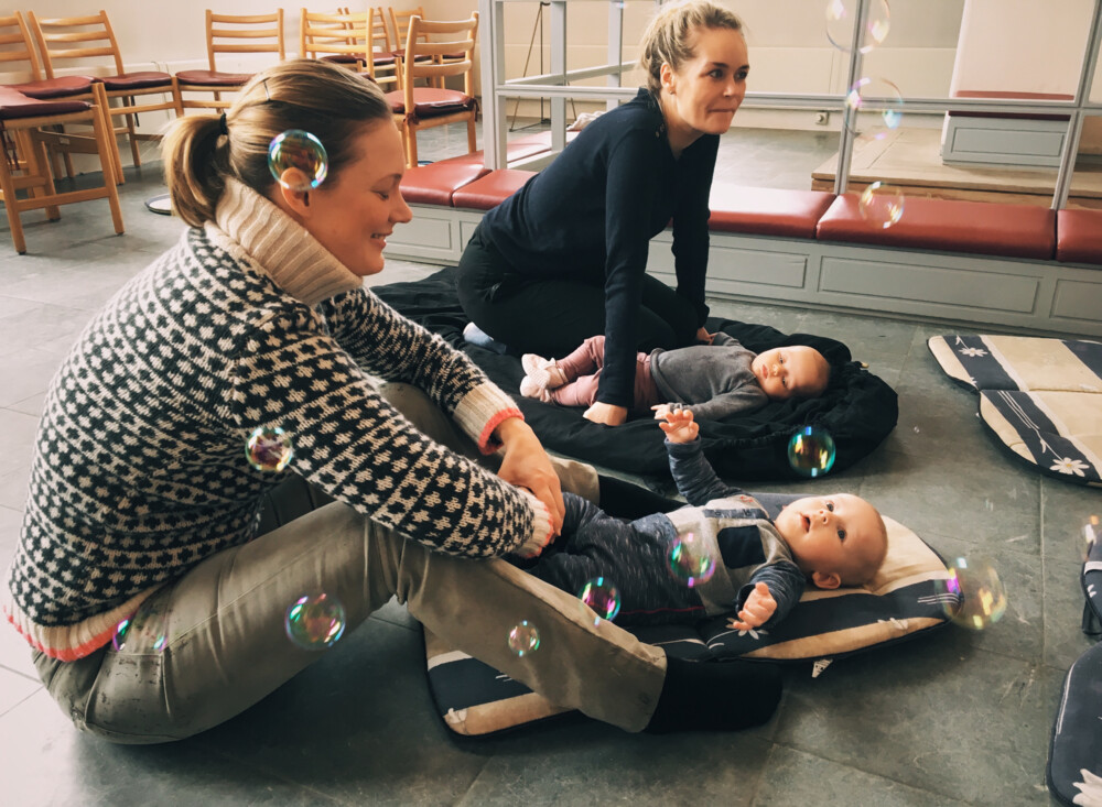 Sæbebobler omkring to kvinder, der sidder på gulv - deres babyer ligger foran dem.