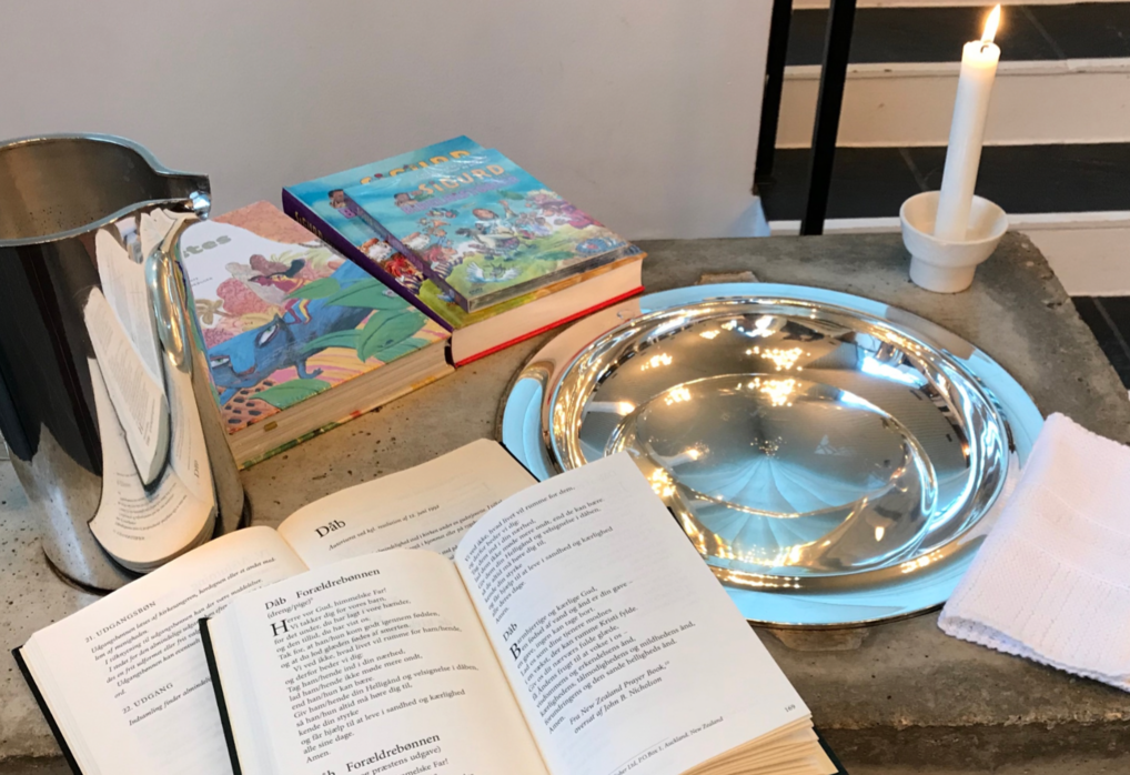 Bøger, kande og stearinlys omkring dåbsfad